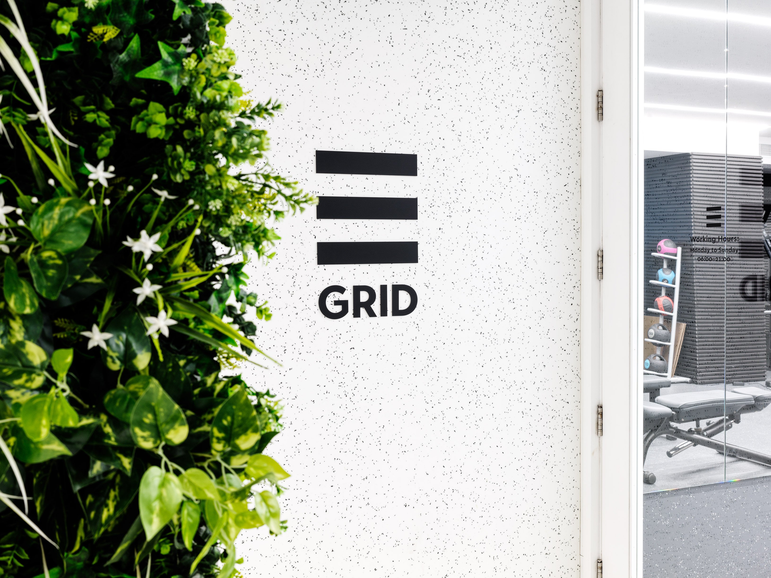 GRID logo on white wall with green vertical plants beside it.