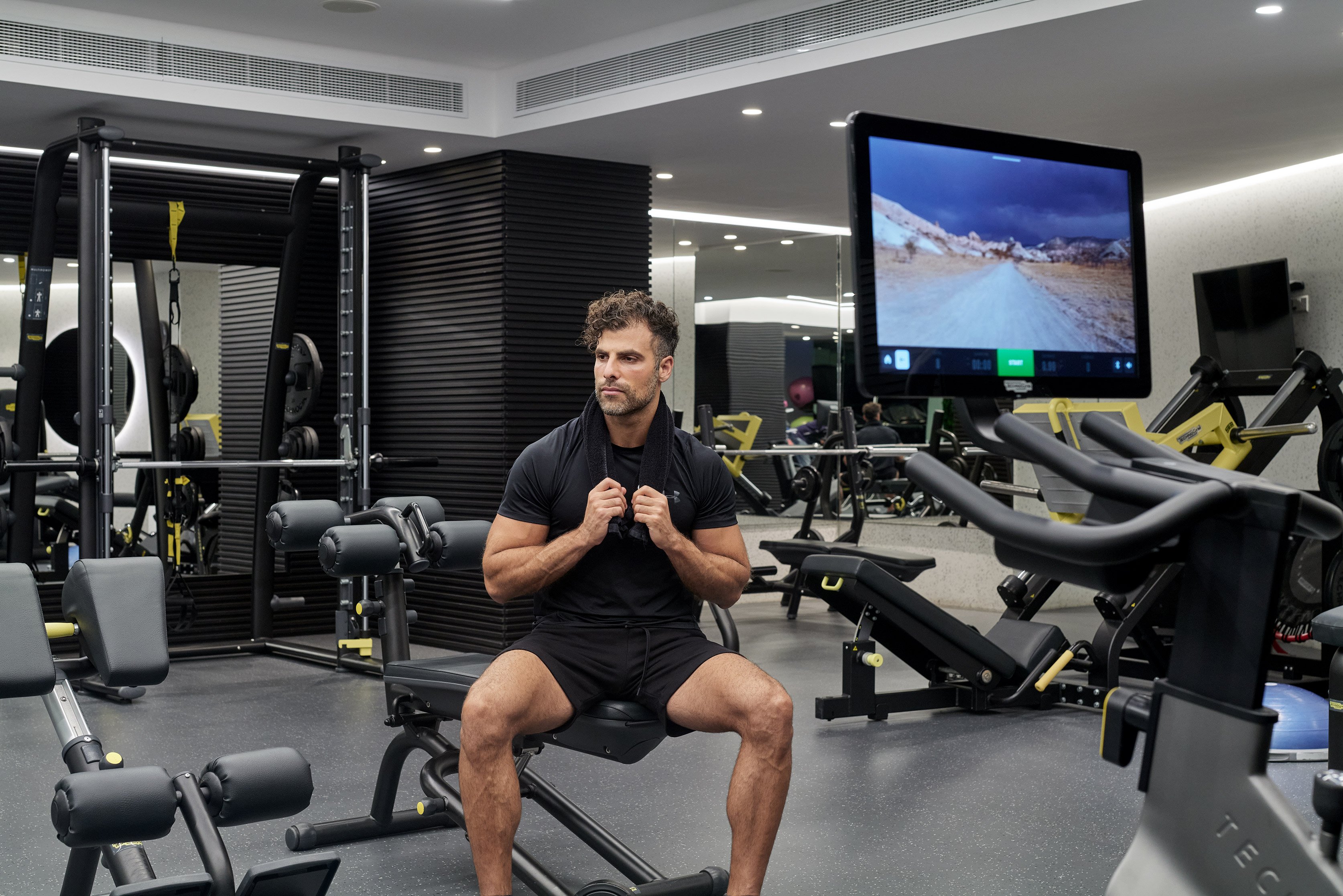 Man training on seated machine in modern fitness room.