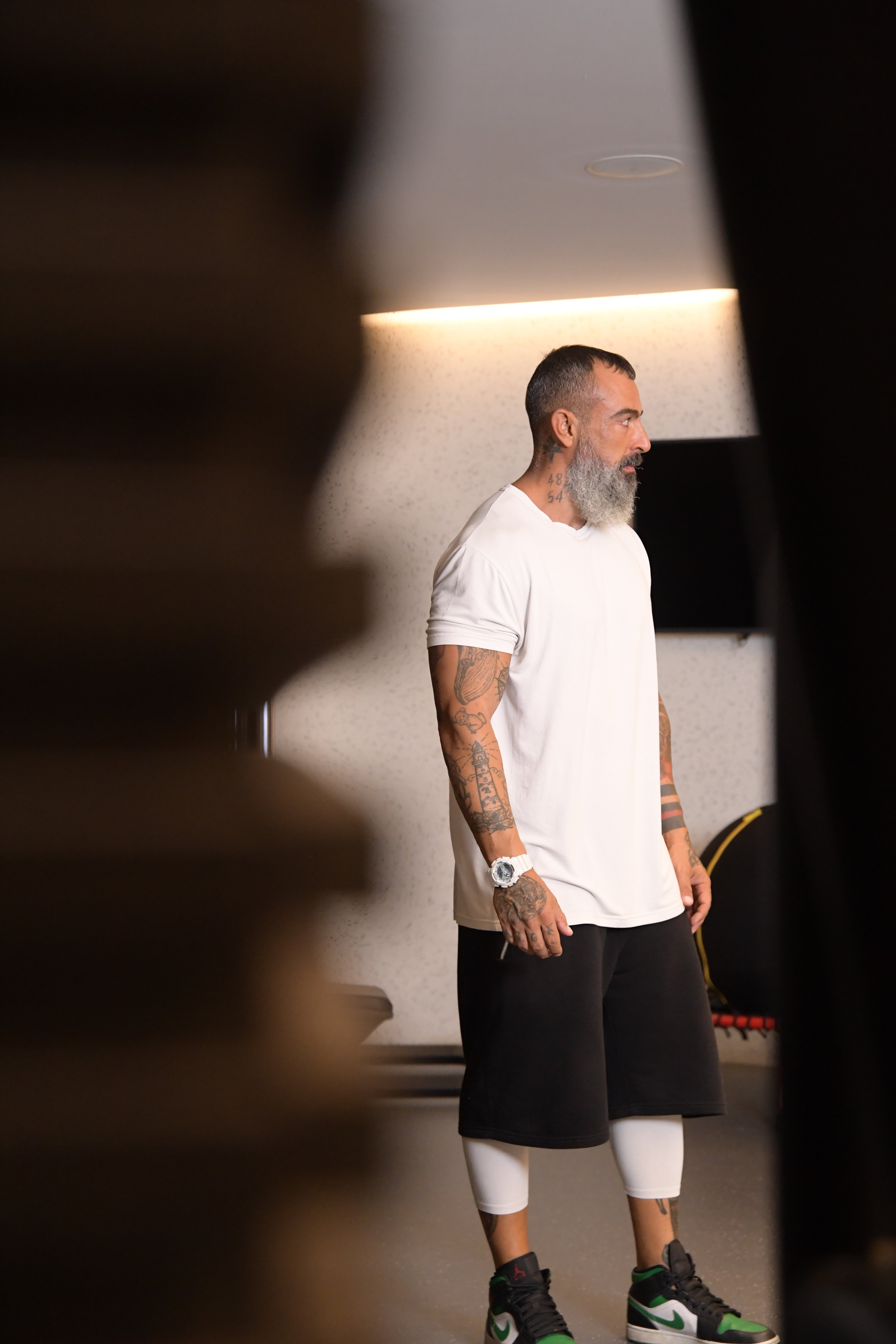 Man with tatoos and sports outfit in the gym, photographed through the entrance door.