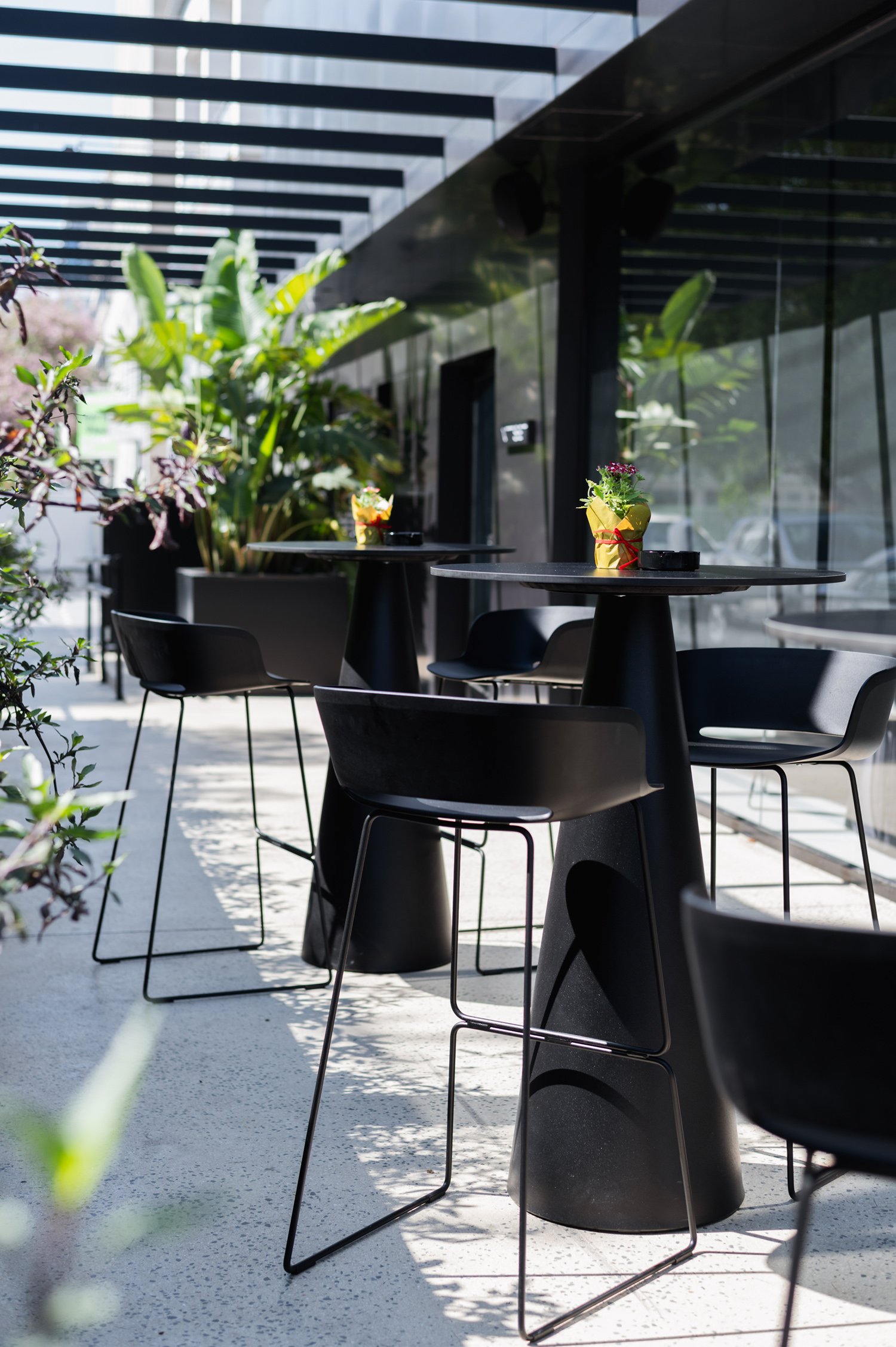 Outdoor terrace with black tables and chairs surrounded by plants.