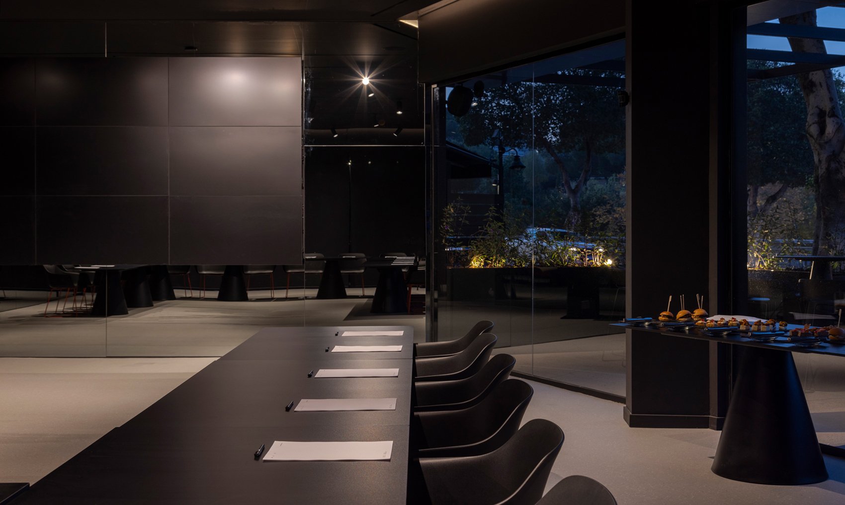 Modern conference space with black furniture and night view through windows.