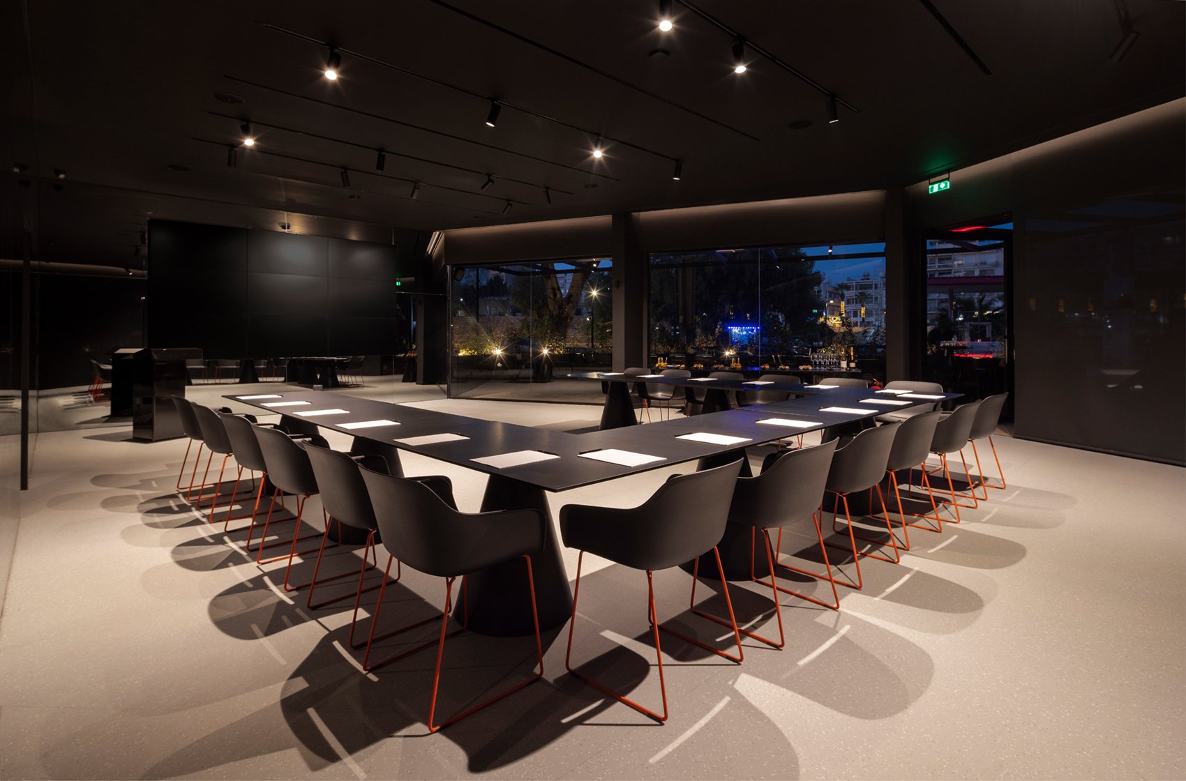 Large meeting room set up with long tables and chairs, evening light outside.