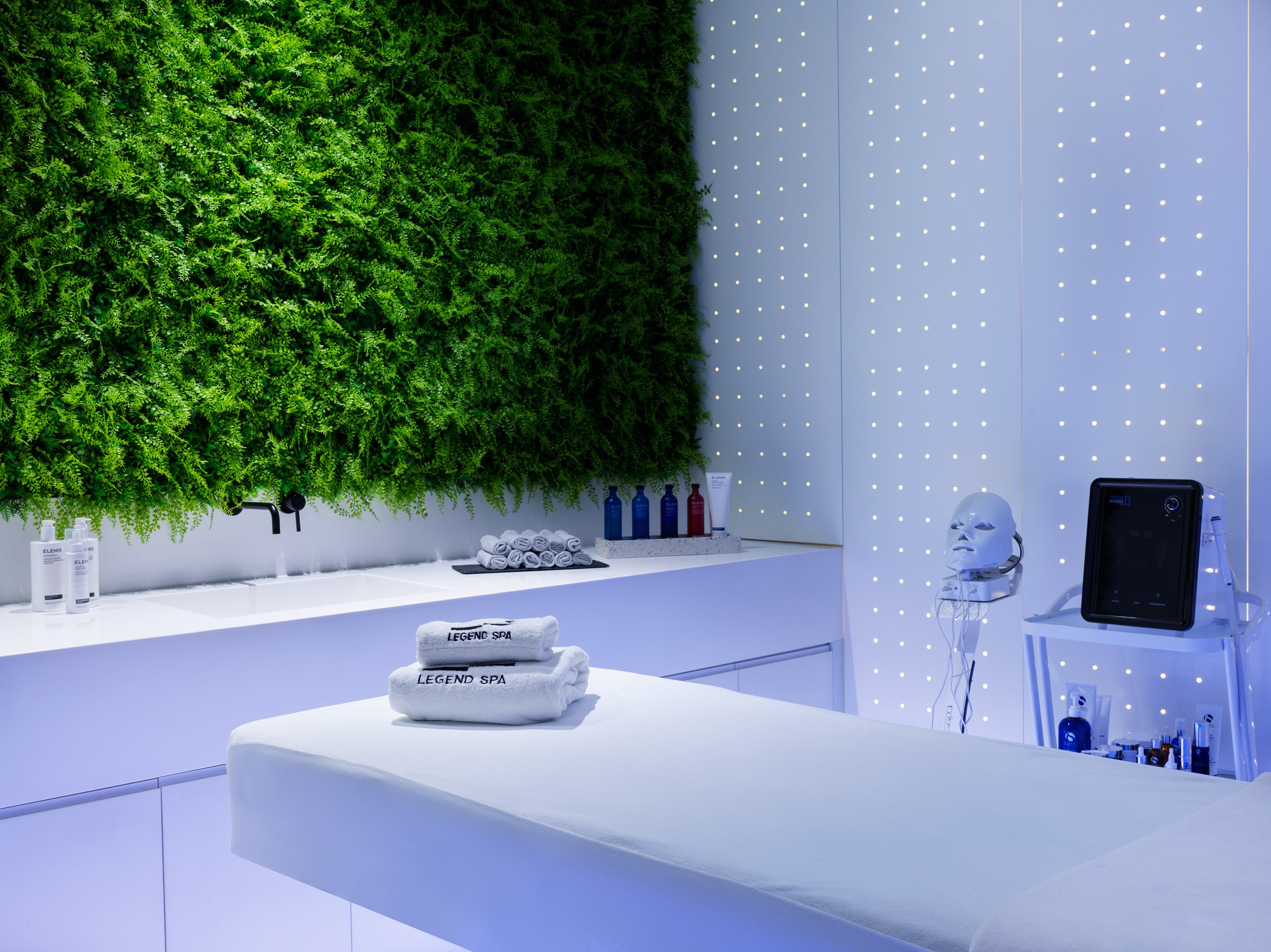 Bright treatment room with massage table and green plant wall.