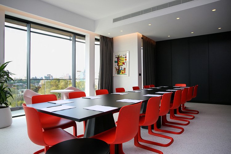 Meeting room with red chairs, large window and dark wall.