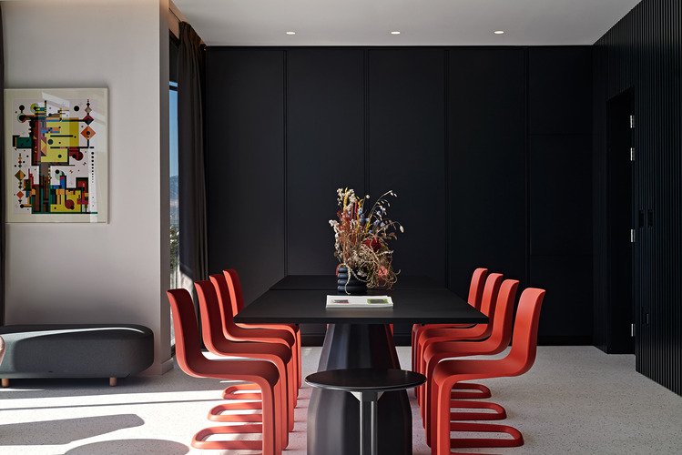 Dining area with red chairs around black table and floral centrepiece.