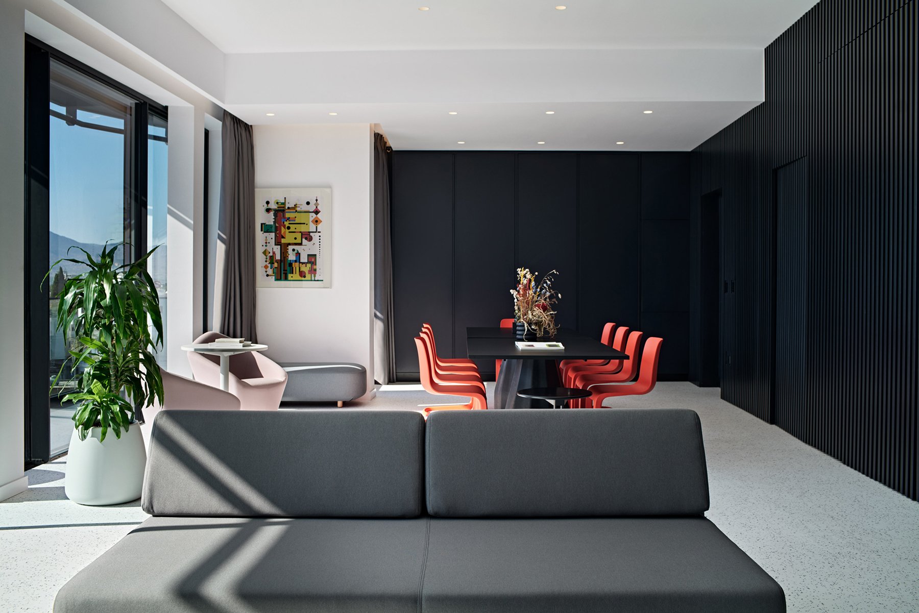 Lounge with grey sofa, red chairs and black wall cabinet.