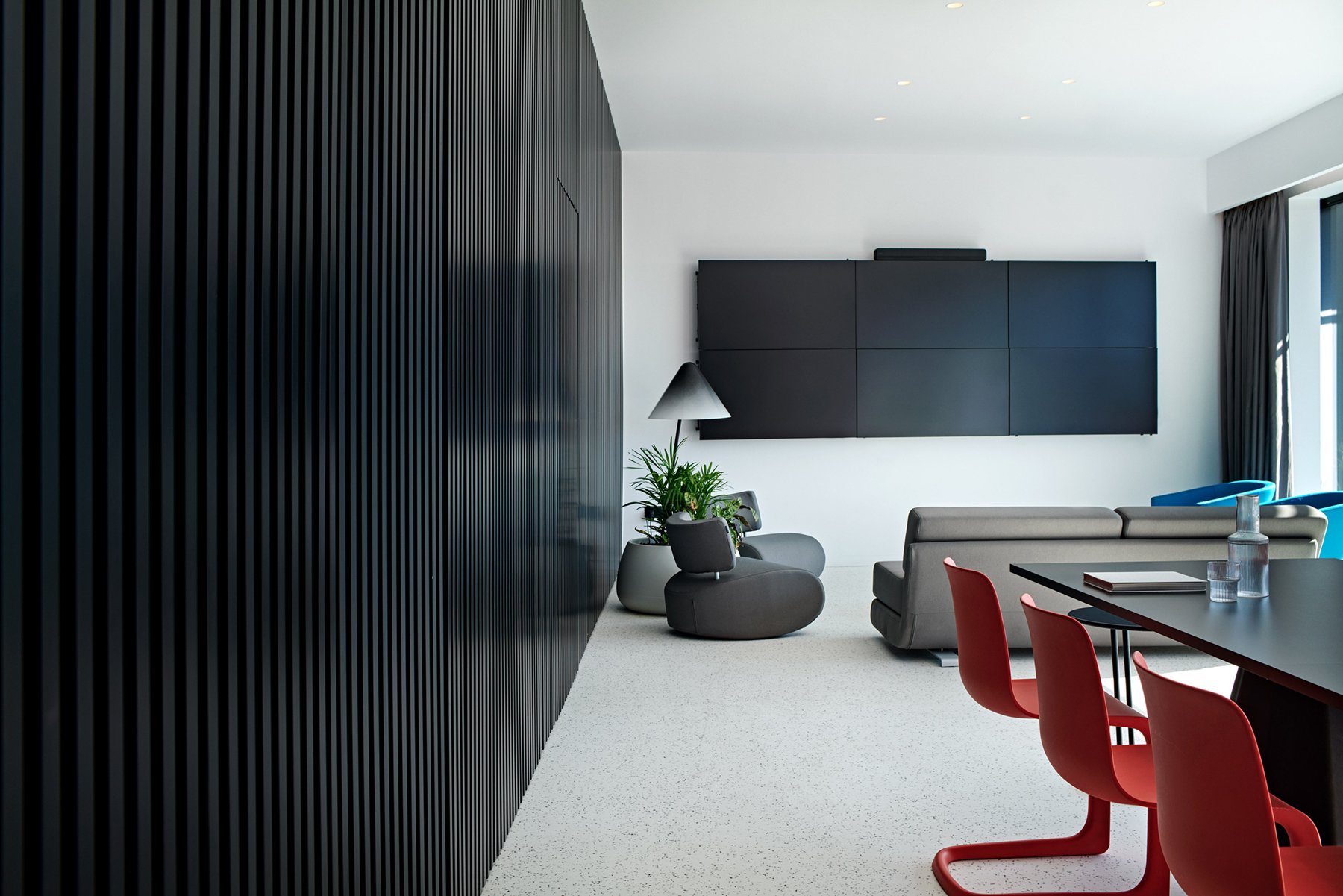 Living area with dark wall panels, grey chair and red dining chairs.