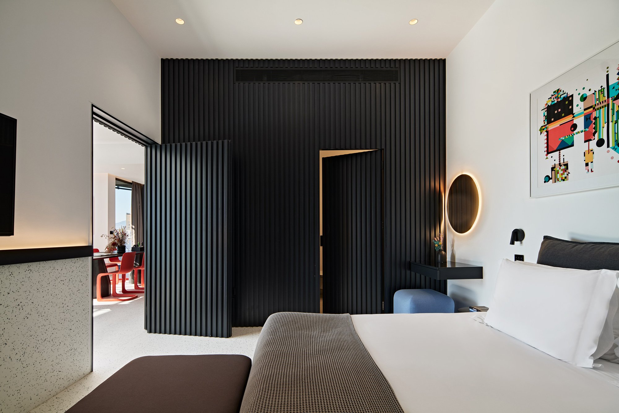 Bedroom with dark feature wall and red chairs in adjoining room.