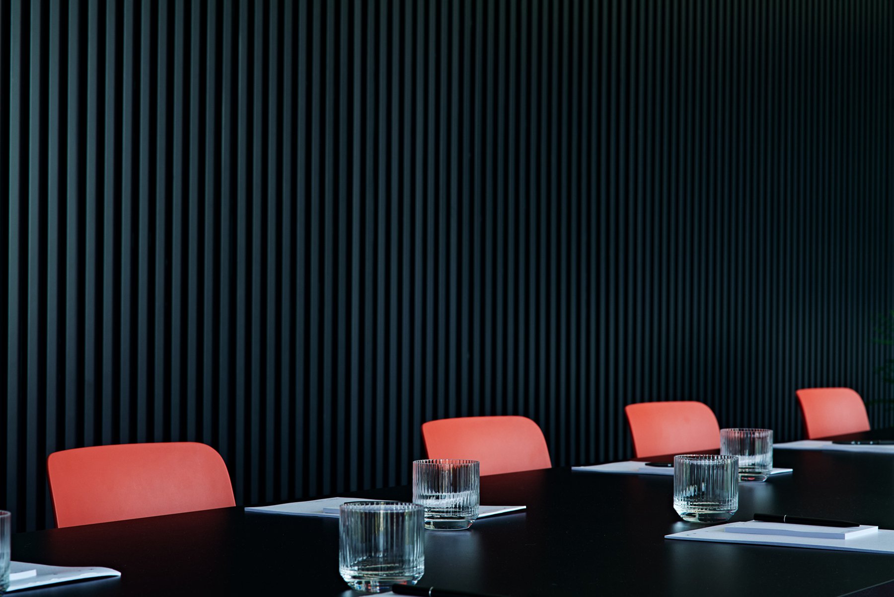 Meeting table set with red chairs, water glasses and black wall behind.