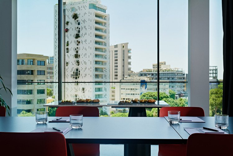 Meeting table set with red chairs, water glasses and black wall behind.
