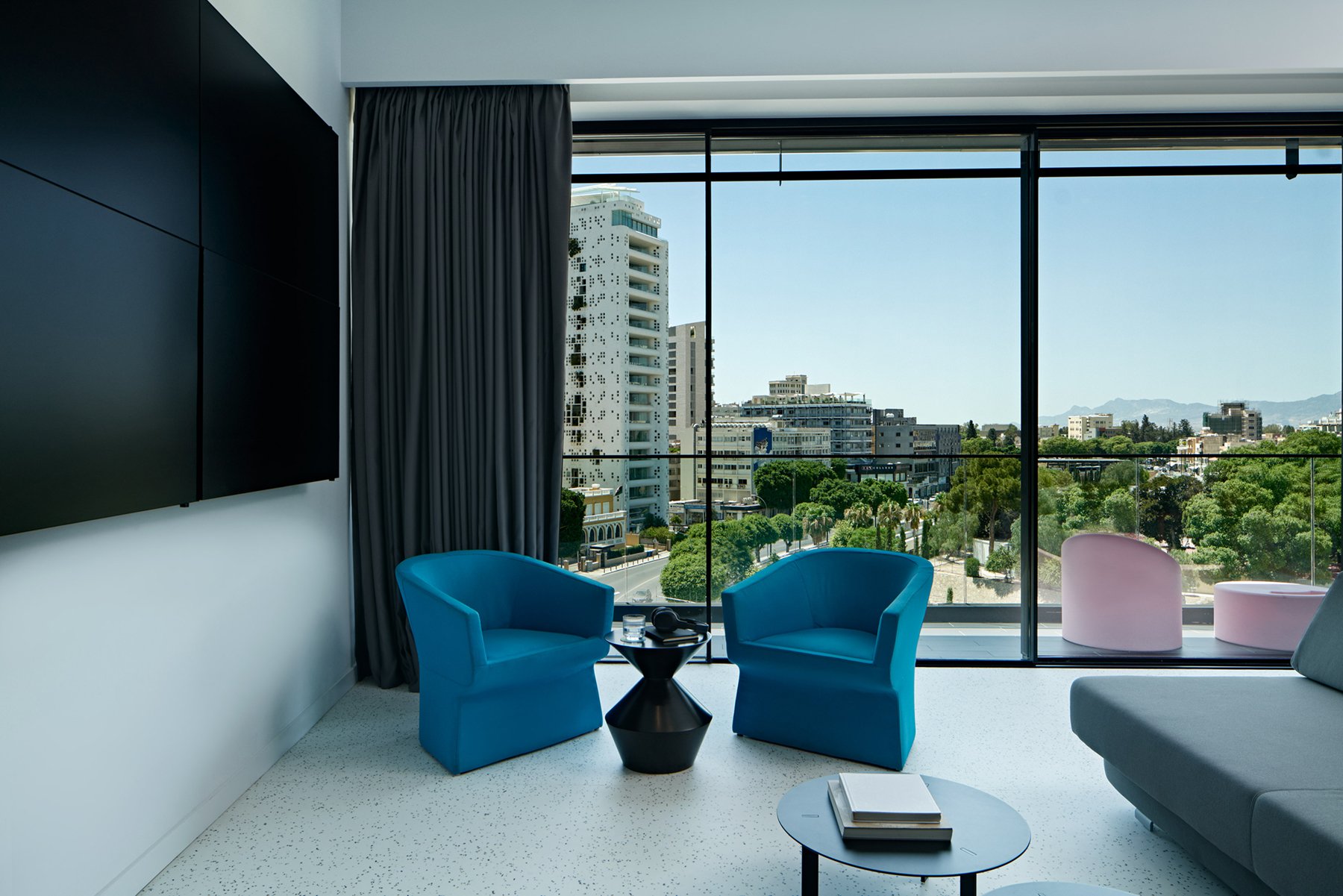 Lounge area with two blue chairs and city view through large window.