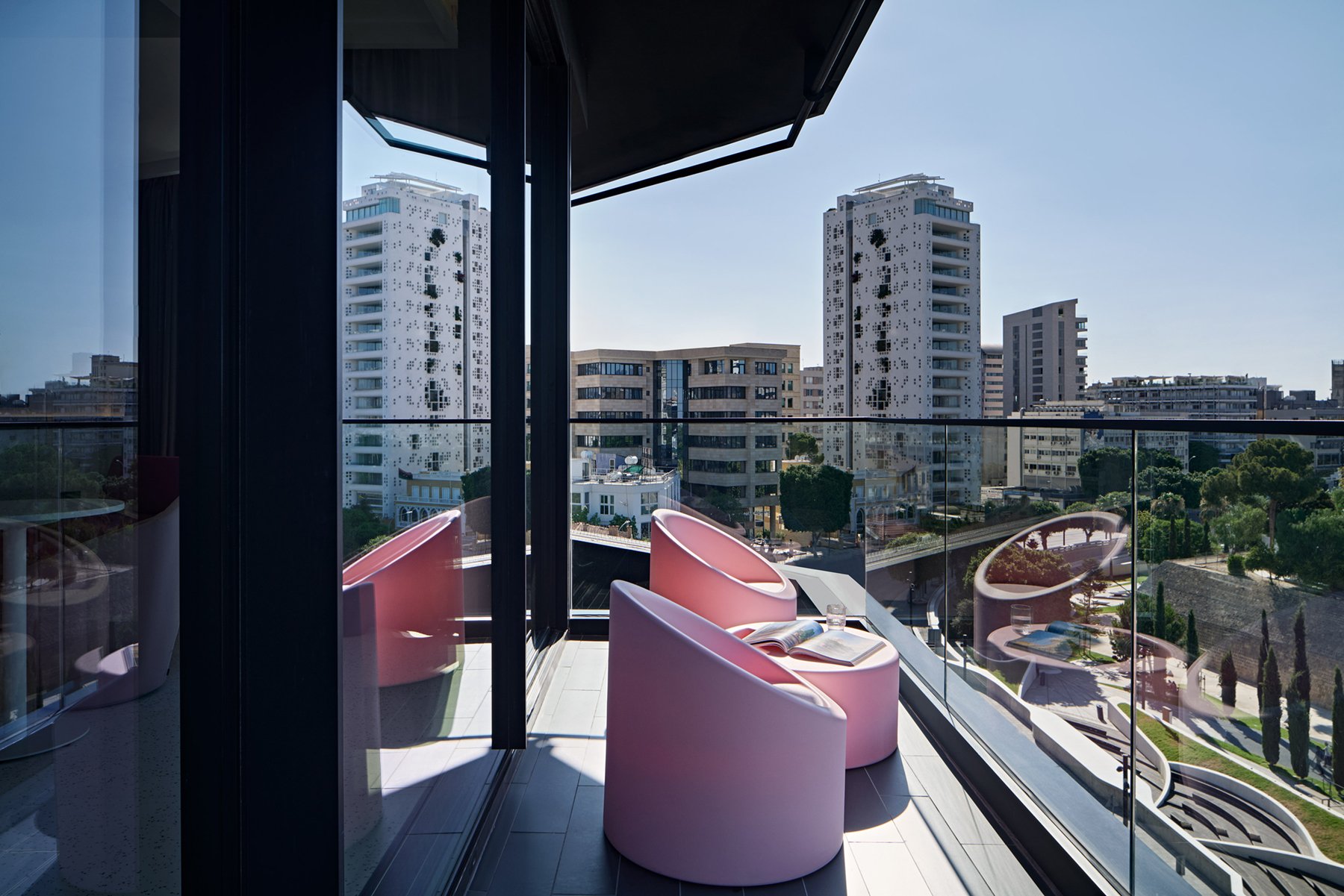 Balcony with pink chairs overlooking city buildings.