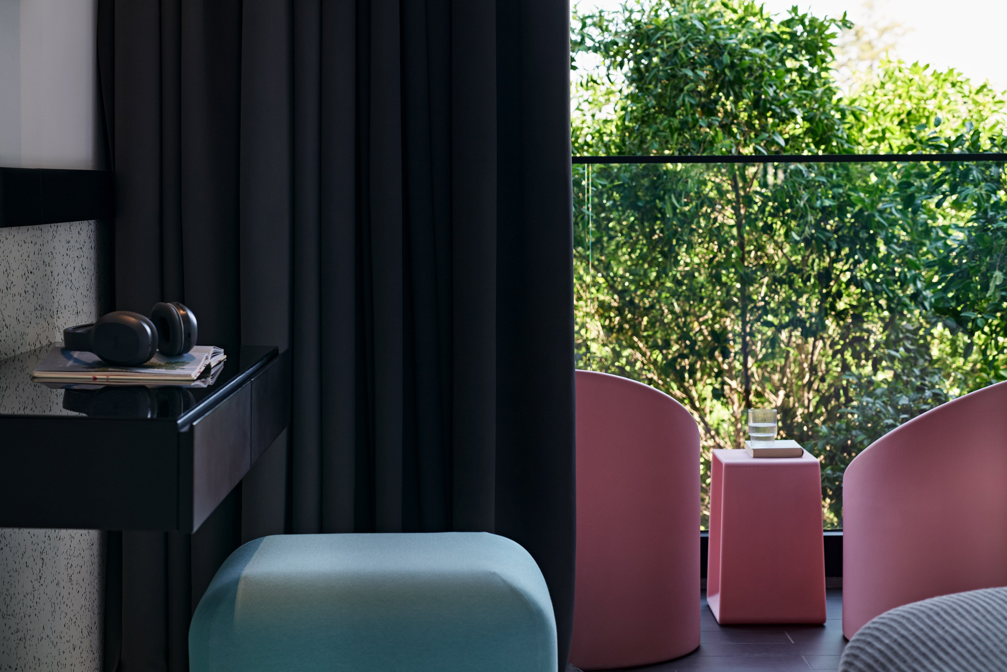 Bedroom corner with black curtains, pastel stool and pink chairs outside.