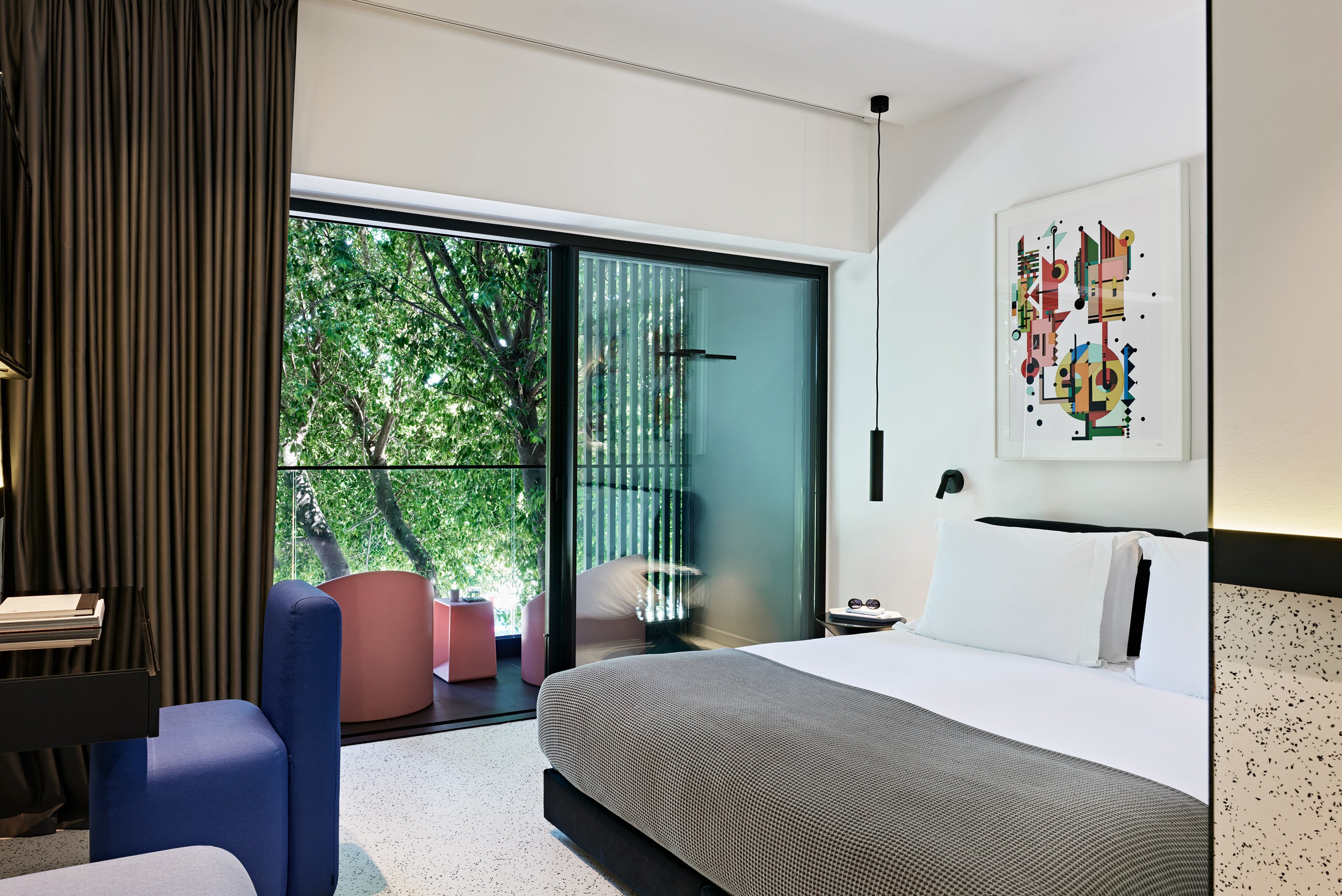 Bedroom with balcony and pink chairs overlooking greenery.
