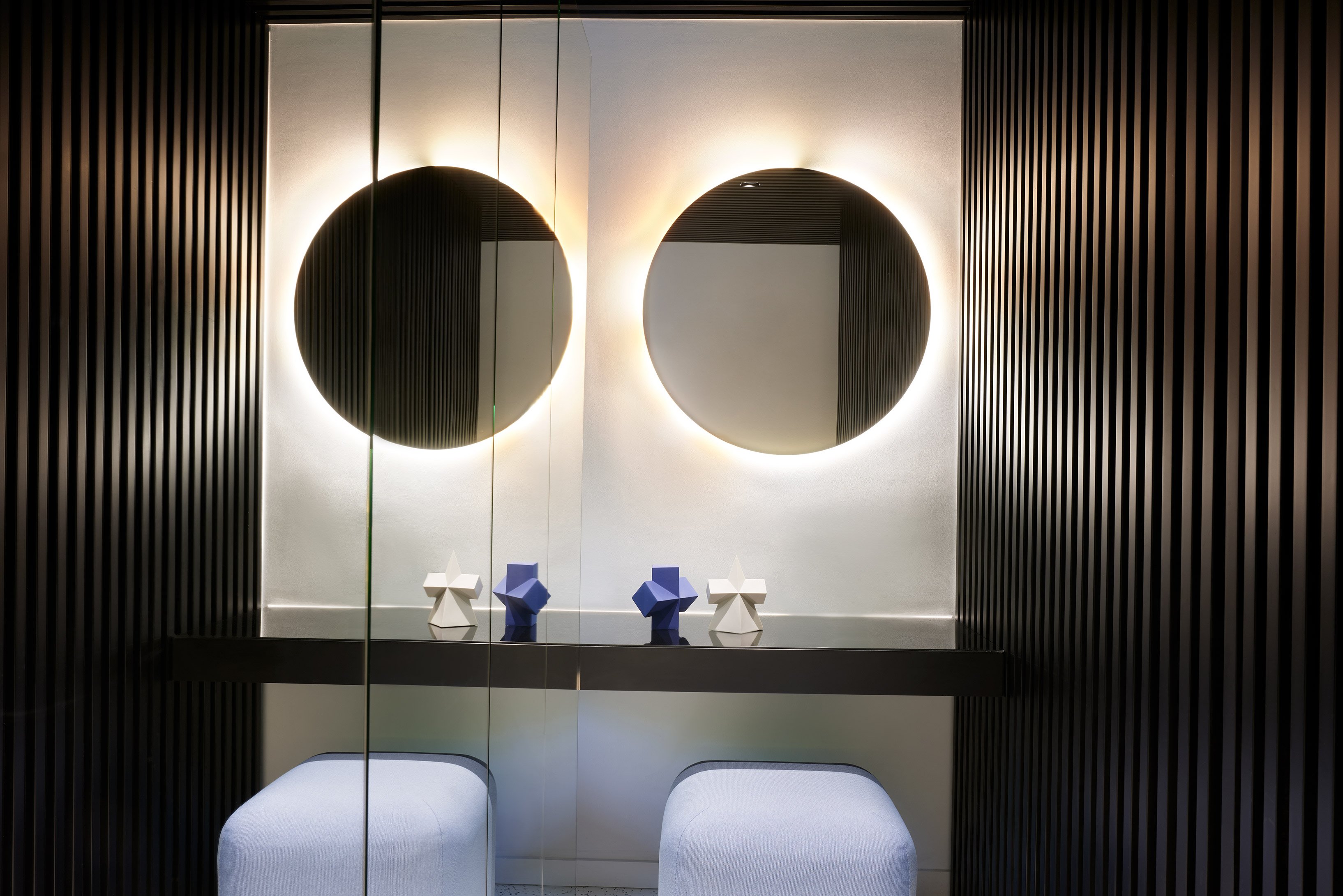 Vanity with round mirrors, black wall and a blue stool.