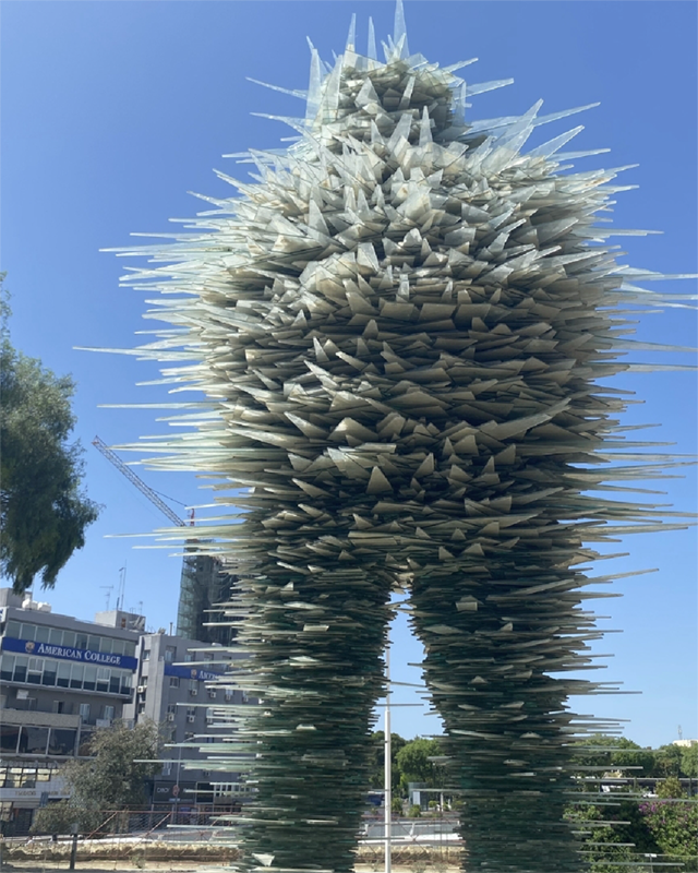 Modern glass sculpture resembling stacked spikes outdoors.