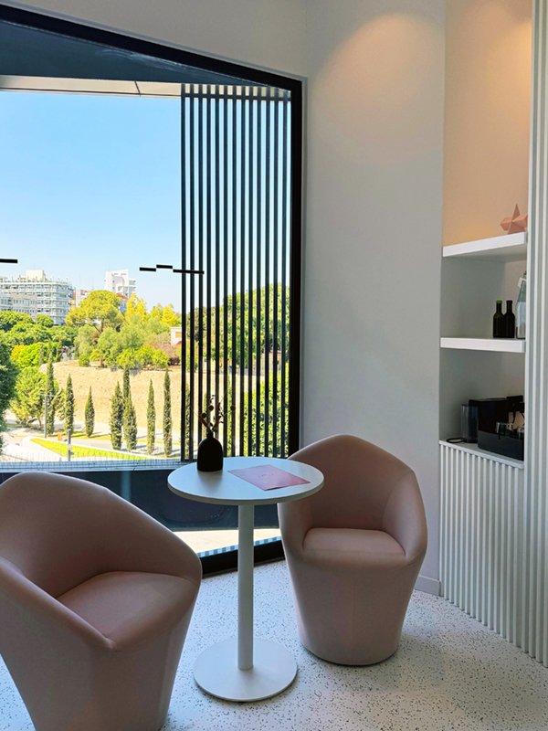 Seating area with beige chair, vase and city view through tall window.