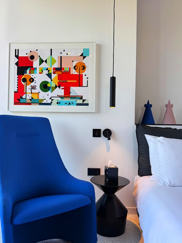 Blue chair beside bed with colourful abstract artwork on the wall.