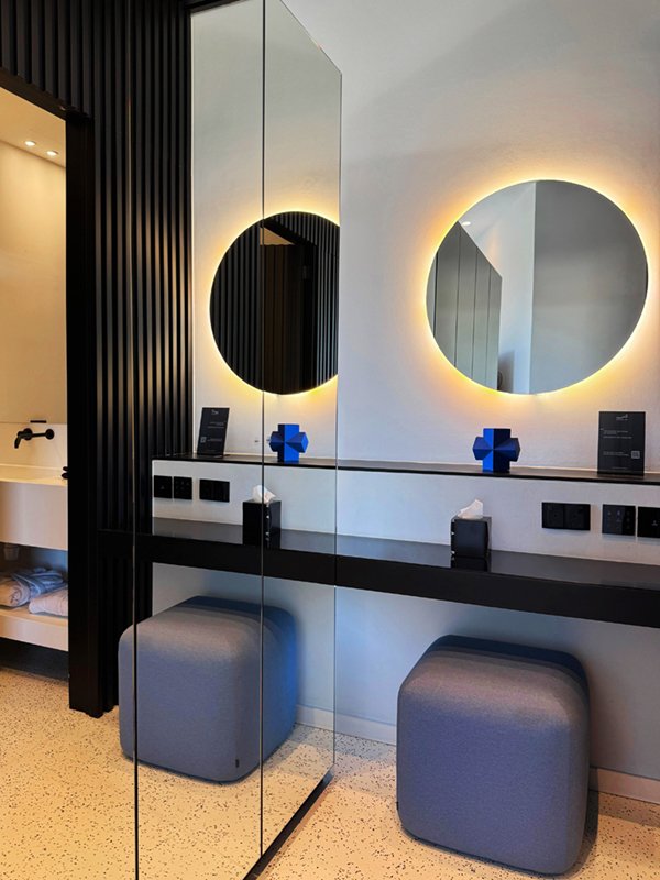 Bathroom vanity with a circular mirror, blue stool and modern lighting.