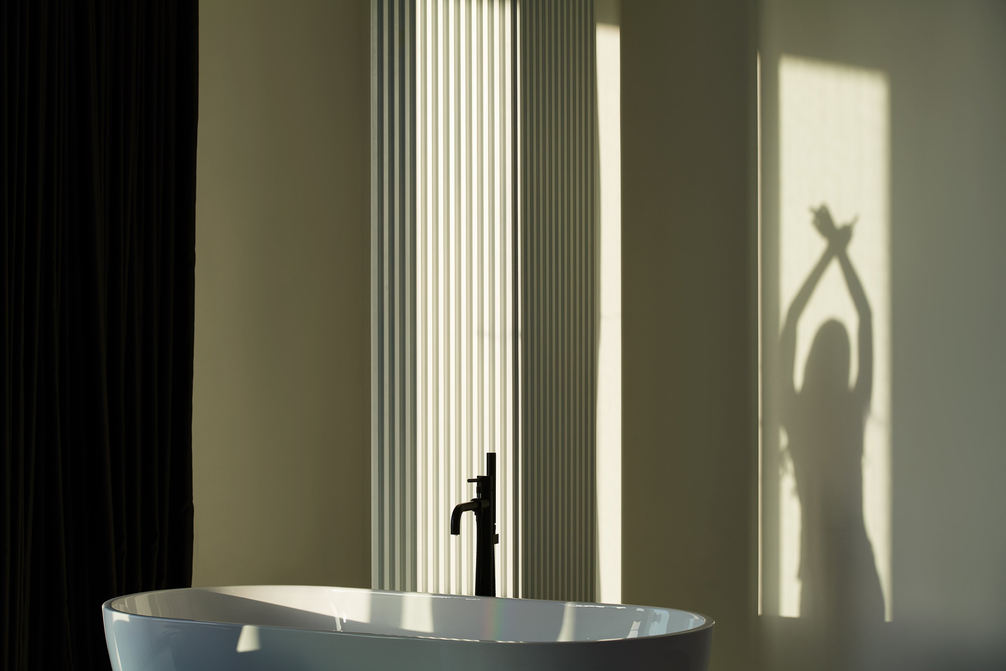White bathtub with black faucet beside ribbed beige wall in soft light.