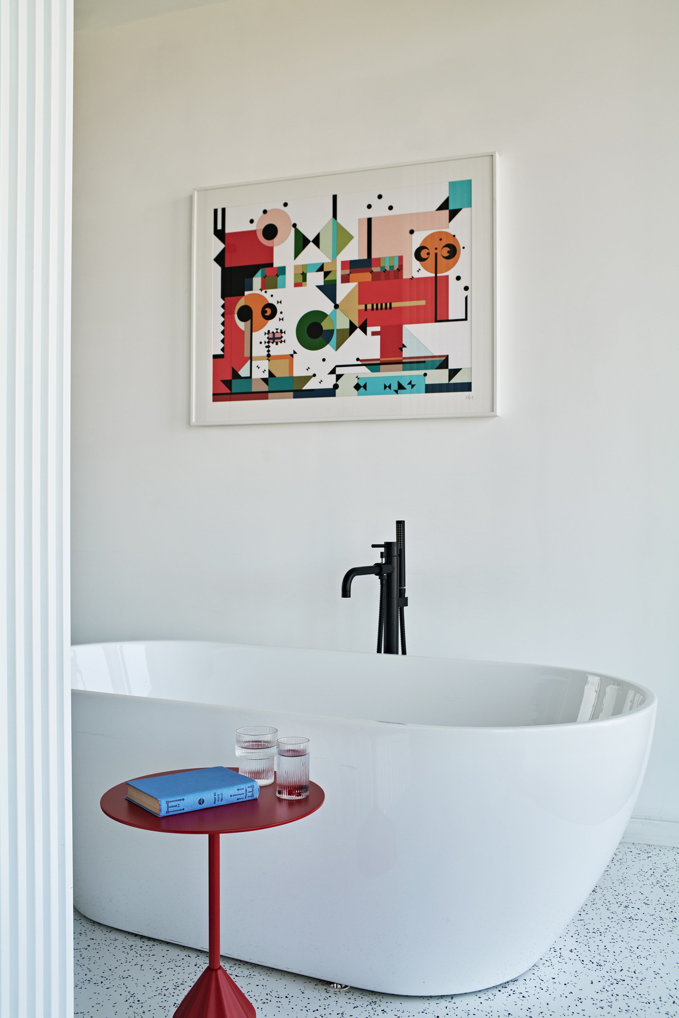 Bathroom detail with bathtub, red table and decorative wall art.
