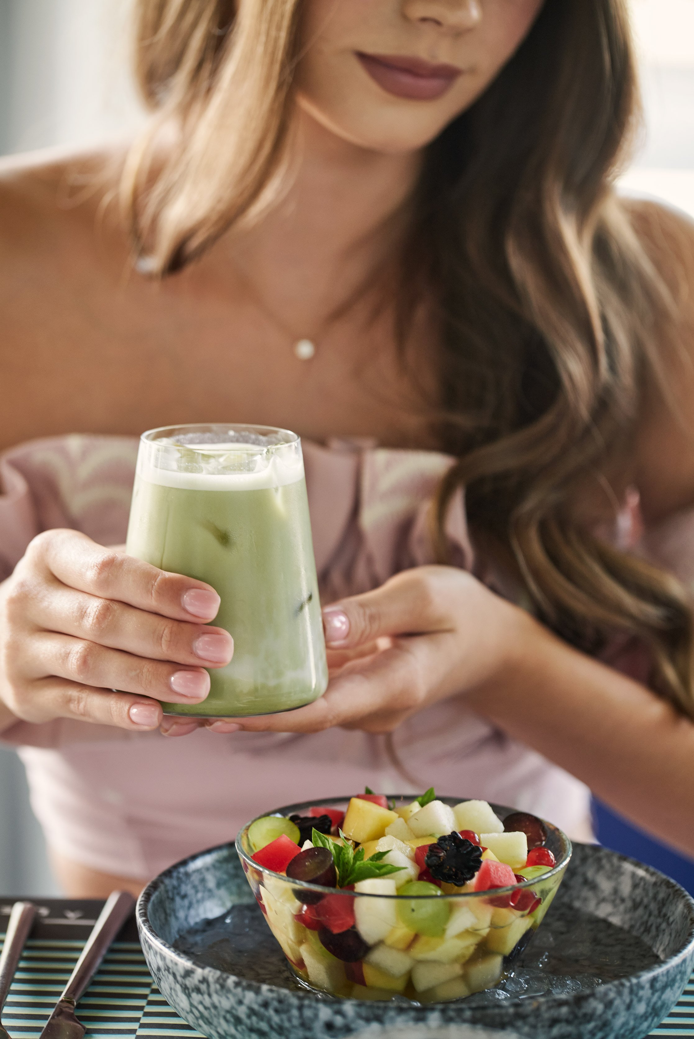 Woman holding a glass of green smoothie and fruit bowl.