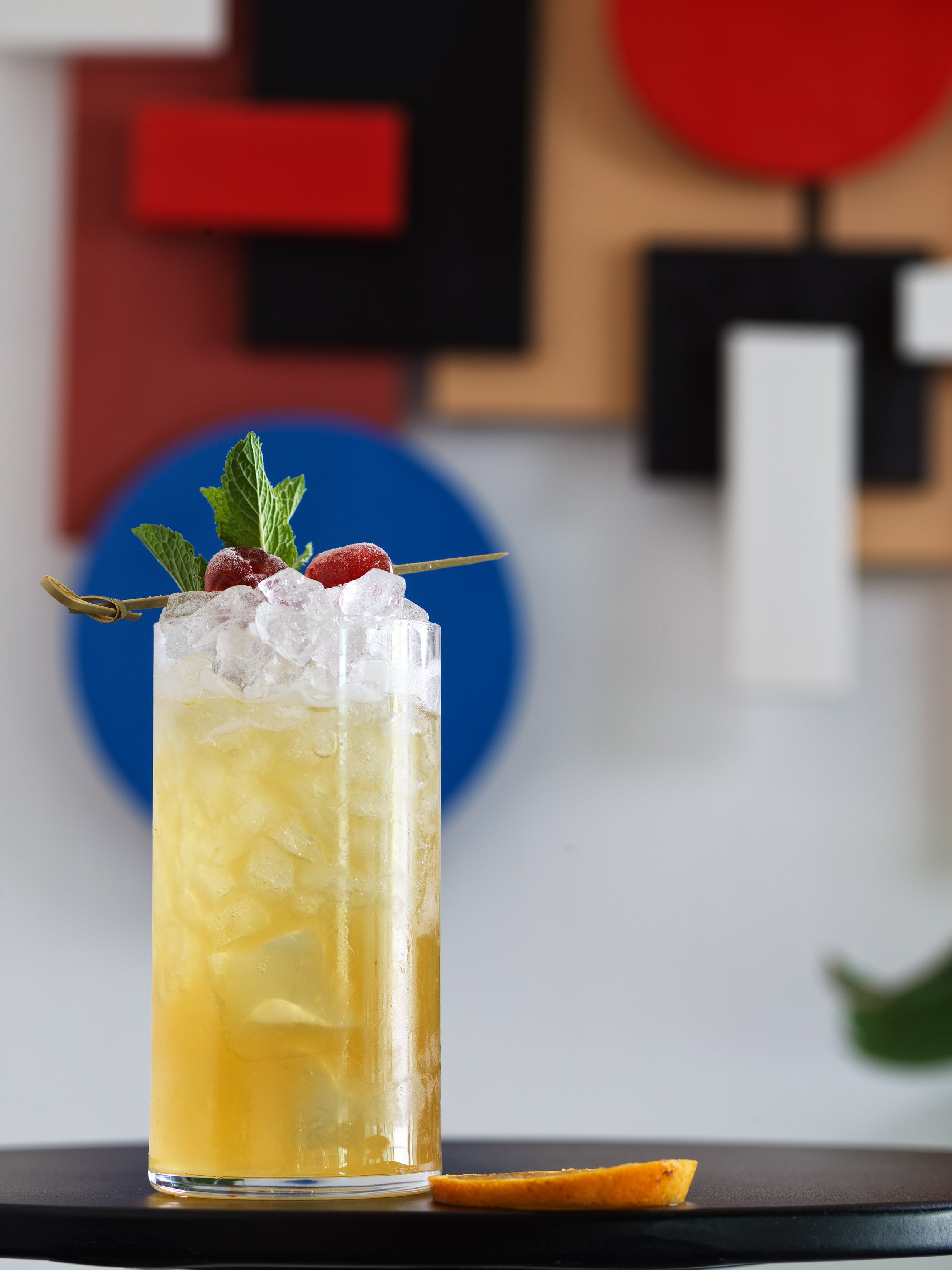 Yellow cocktail with mint and peach slice on dark table.