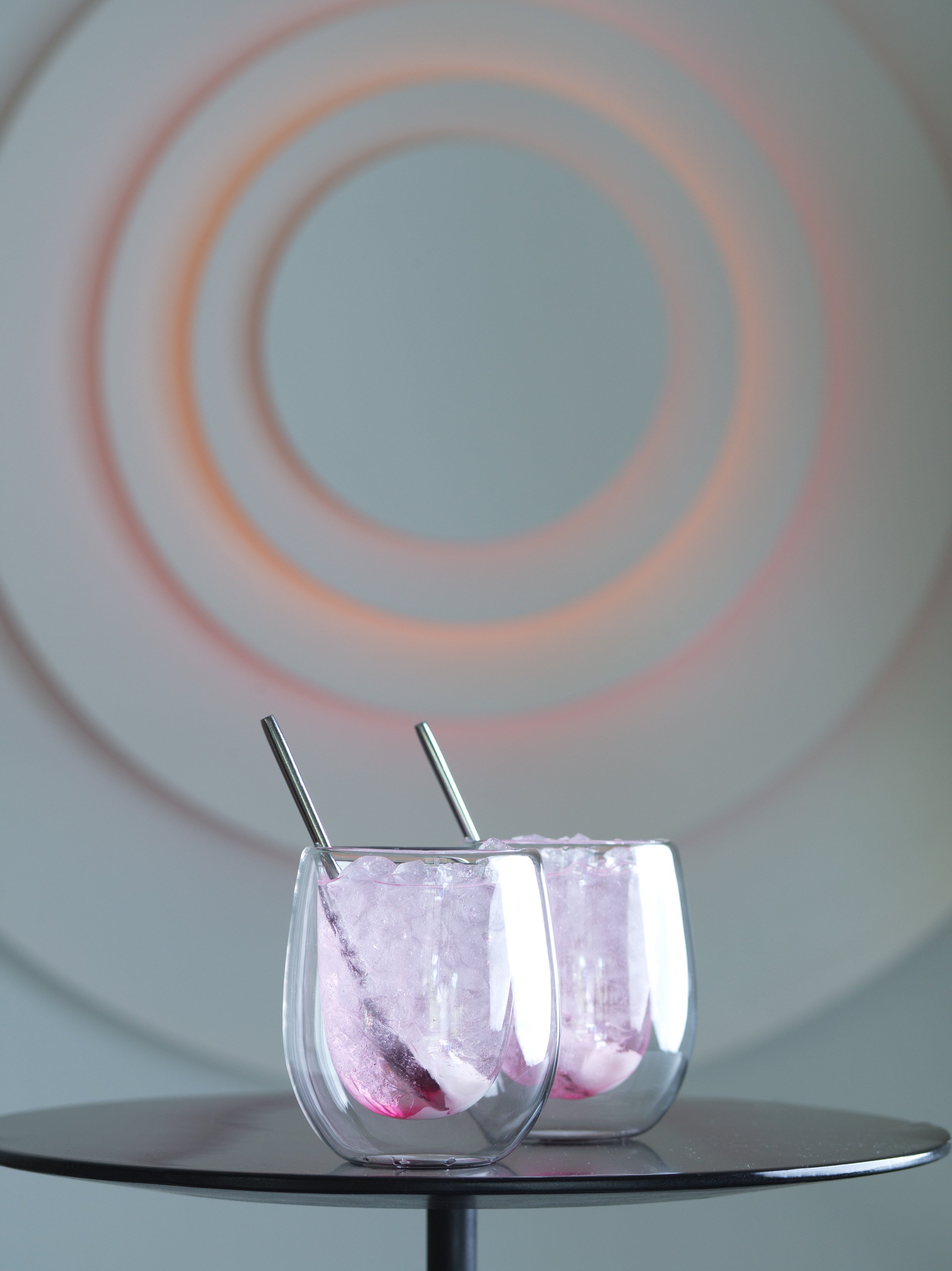 Two gin and tonic glasses with ice on marble surface.