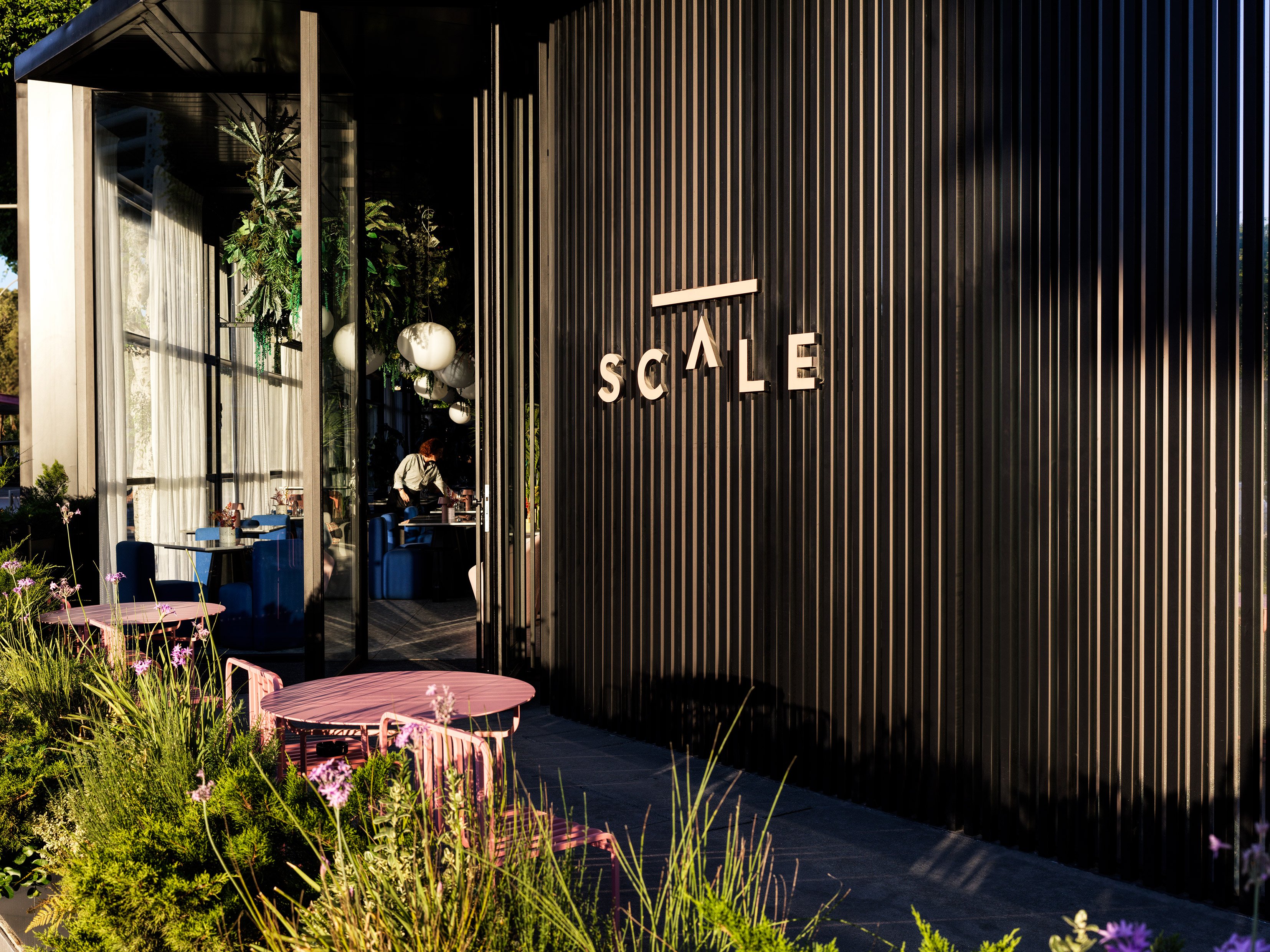 Exterior view of SCALE restaurant entrance with plants and terrace.