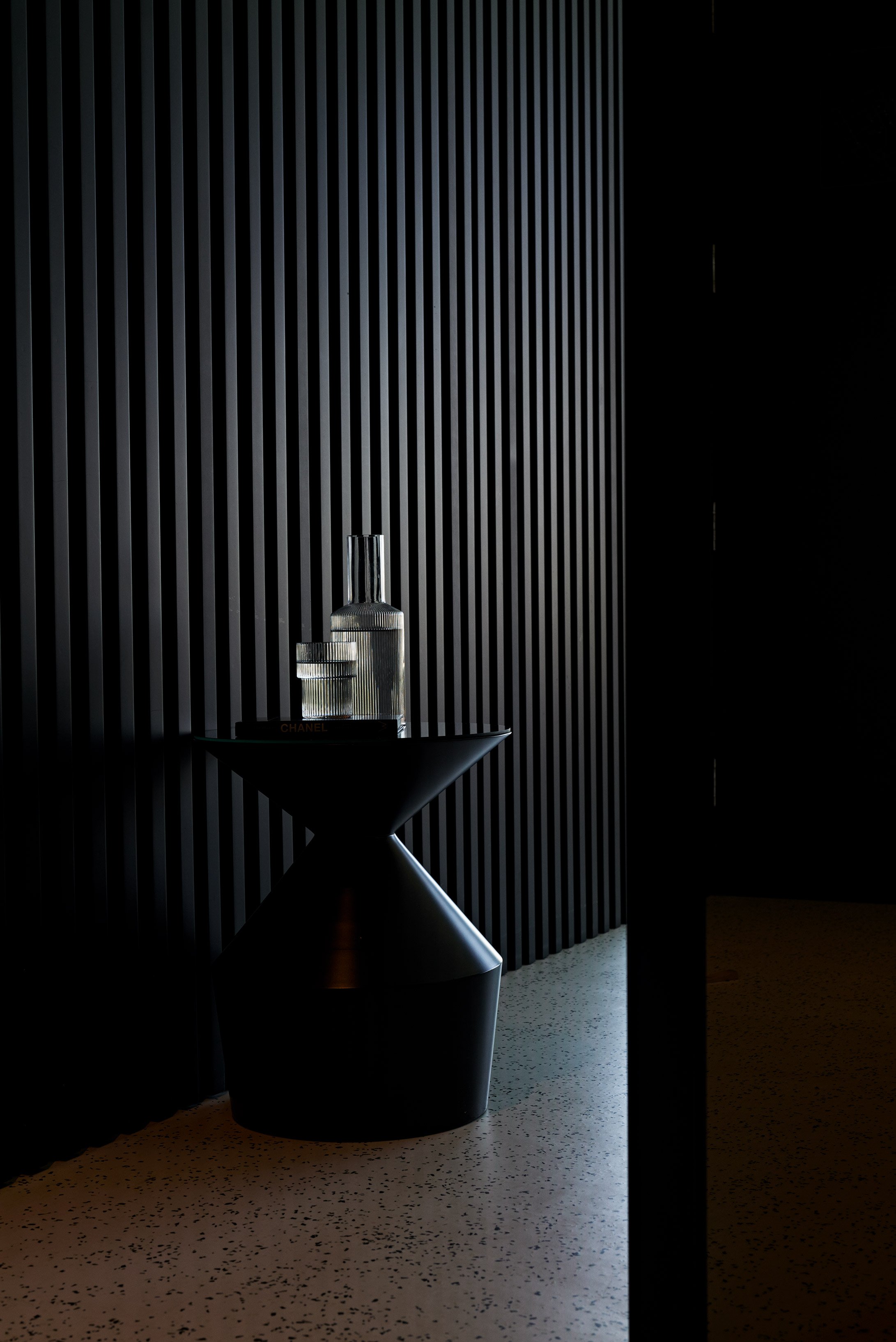 Minimalist hotel room with water on a black tiny table and black wall.