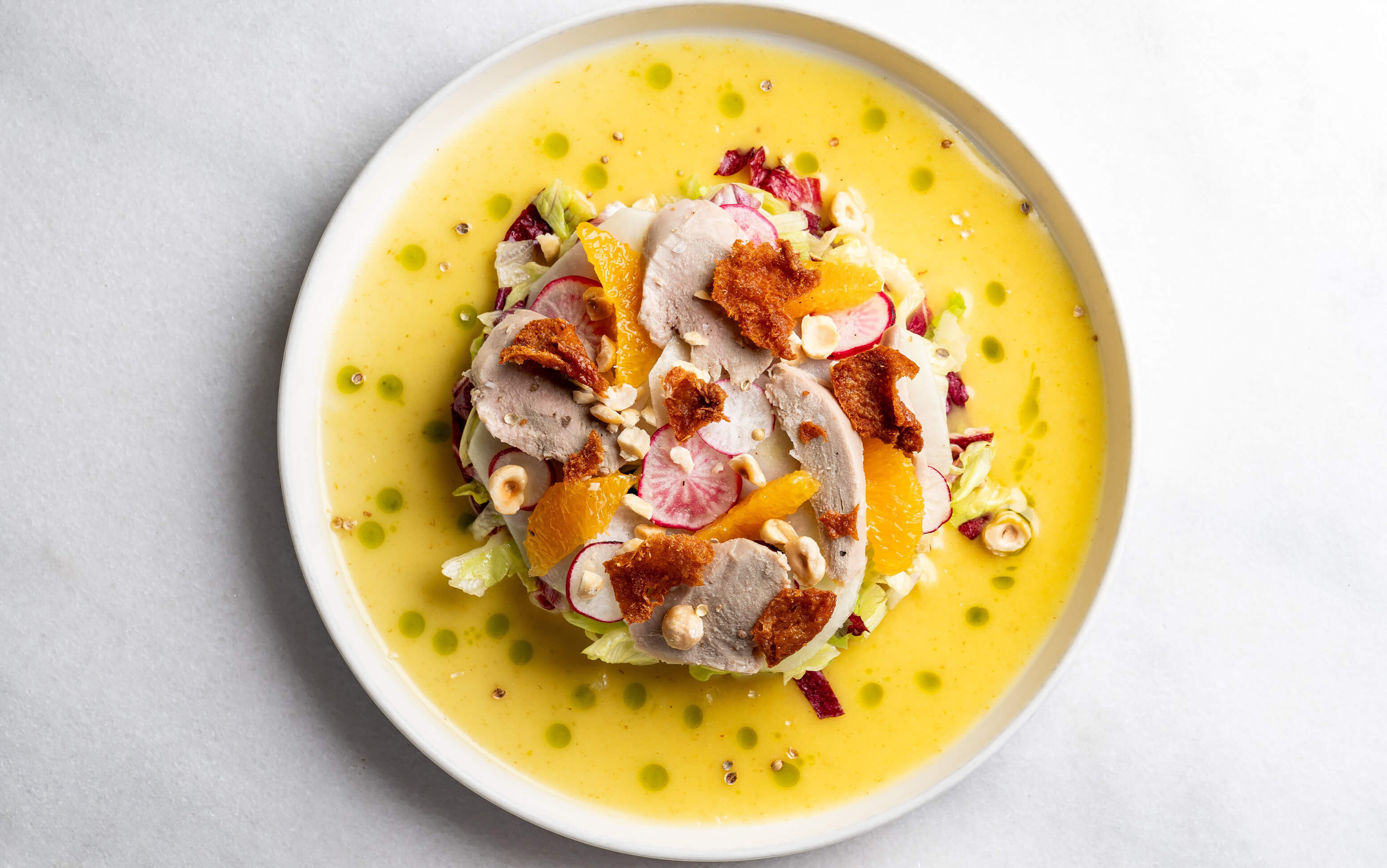 Colorful soup with vegetables and crispy toppings served in a white bowl.